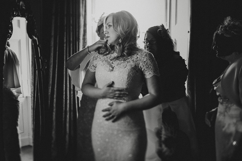 black and white photo of bride getting getting her dress buttoned up by mother
